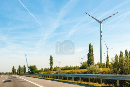Photo for Unique view from the large highway at large park of wind turbines producing electricity above forest with crane installing another one in background - Royalty Free Image