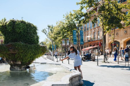 Photo for Aix-en-Provence, France - Jul 17, 2014: People pass leisurely in the hot sun of Cours Mirabeau, Aix-en-Provence. Trees and The Fountain des Neufs Canons grace a unique town plaza surrounded by - Royalty Free Image