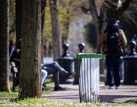Foto de Un fin de semana en un parque público urbano revela siluetas de personas y un bote de basura: medidas de la ciudad para reciclar o eliminar adecuadamente para el medio ambiente. - Imagen libre de derechos