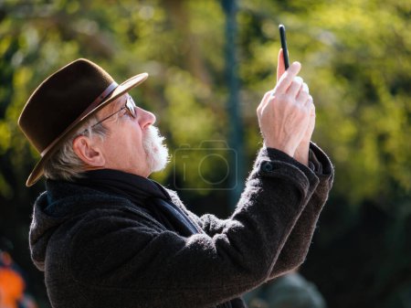 Foto de Strasborg, Francia - 29 de marzo de 2023: Un hombre mayor en Alsacia, Francia, está haciendo turismo mientras toma una foto. Lleva ropa tradicional y un sombrero, disfrutando de la actividad de descubrir nuevos lugares. - Imagen libre de derechos