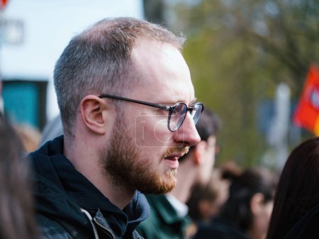 Foto de Strasborg, Francia - 29 de marzo de 2023: Un joven adulto con barba y gafas sonríe calurosamente en este retrato de cerca en una protesta - Francia experimenta semanas de protestas y acciones de huelga relacionadas con un - Imagen libre de derechos