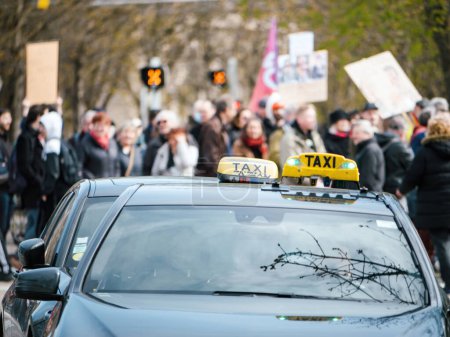 Téléchargez les photos : Voitures de taxi garées dans la rue avec une silhouette de manifestants personnes en arrière-plan - pancartes et drapeaux dans leurs mains - en image libre de droit