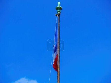 Foto de El cielo azul claro está salpicado con la bandera nacional francesa, su polo que alcanza alto desde una vista de ángulo bajo. Patriotismo irradia en su ausencia de personas y presencia de una luz de calle. - Imagen libre de derechos