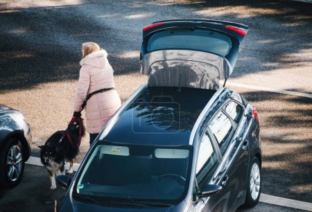 Photo for Germany - February 10, 2023: A woman and her dog are exiting a motor vehicle in an outdoor setting, with the open trunk above their view. - Royalty Free Image