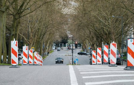 Téléchargez les photos : Strasbourg, France - 29 mars 2023 : Une avenue ensoleillée à Strasbourg, France avec des rayures sur la route et des panneaux indiquant un projet de réparation. Un arbre offre de la verdure le long de la rue animée de la ville. - en image libre de droit