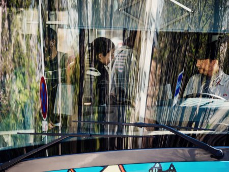 Téléchargez les photos : Strasbourg, France - 29 mars 2023 : Un chauffeur d'autobus accueille les passagers dans une gare urbaine pour leur voyage et leur transport dans une ville animée remplie de reflets dans les gaz des arbres et - en image libre de droit
