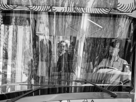 Téléchargez les photos : Strasbourg, France - 29 mars 2023 : Un chauffeur d'autobus accueille chaleureusement les passagers dans une gare urbaine, un paysage urbain animé reflété dans le verre des arbres et des bâtiments. Un monochrome noir et blanc classique - en image libre de droit