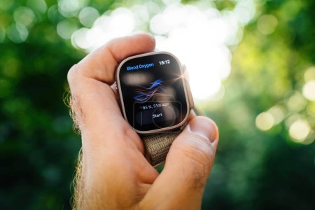 Foto de Londres, Reino Unido - 28 de septiembre de 2022: Nuevo reloj de titanio Apple Watch Ultra diseñado para actividades extremas en mano de atleta masculino con medición de oxígeno en la sangre en la retina muestra hermoso jardín bokeh - Imagen libre de derechos
