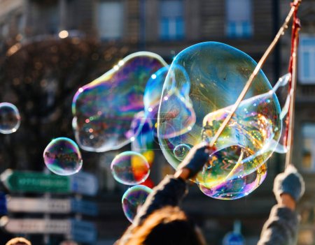 Foto de Un enorme grupo de personas en una vista trasera, sus manos levantadas y soplando burbujas de jabón brillante que flotan en el aire, creando una fragilidad y burbuja líquida. - Imagen libre de derechos