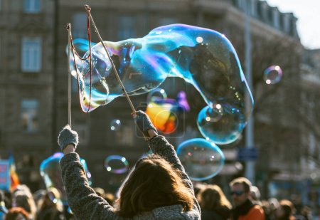 Foto de Un grupo de personas está creando enormes burbujas de jabón brillantes en el aire con una varita de burbujas, maravillándose de la fragilidad y la belleza de estas creaciones líquidas que soplan en el aire. - Imagen libre de derechos