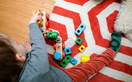 Photo for A cheerful baby plays with colorful wooden toys in a cozy childrens room, lying on the floor surrounded by by colorful toys in different shapes - Royalty Free Image