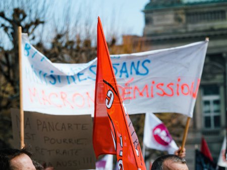 Foto de Strasborg, Francia - 29 de marzo de 2023: Un grupo de manifestantes adultos se reúne frente a un gran edificio arquitectónico, con banderas y pancartas con texto protestando contra la reforma de las pensiones - Imagen libre de derechos