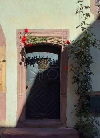 Foto de Un edificio de época en Alsacia, Francia con una brillante flor de rosa y signo de bienvenida a casa. Exterior iluminado por el sol añadiendo encanto al concepto de inversión inmobiliaria. - Imagen libre de derechos