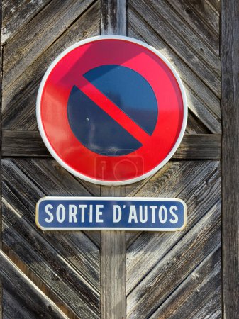 Foto de Un letrero rojo vintage advierte de la salida de coches en un garaje urbano moderno, su entrada a la ciudad francesa iluminada por la luz y rodeada por una puerta de madera - Imagen libre de derechos