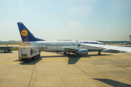 Foto de Alemania - 6 de julio de 2015: Un Boeing 737-MSN 25149 de Lufthansa está llegando a una pista de aterrizaje del aeropuerto, su sombra aparece en la pista mientras un camión SkyChefs descarga y carga para su destino en Alemania. - Imagen libre de derechos