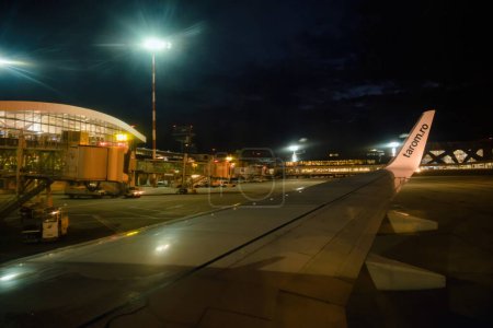 Téléchargez les photos : Francfort, Allemagne - 3 juil. 2015 : Le ciel du soir est illuminé par les lumières de l'aéroport de Francfort. Une aile d'avion de Tarom Airlines attend le départ sur le tarmac pendant que l'éclairage puissant guide les voyageurs à - en image libre de droit