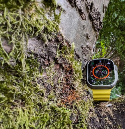 Foto de Londres, Reino Unido - 23-sep-2022: Un nuevo Apple Watch Ultra de titanio diseñado para actividades extremas como los deportes de resistencia brilla en la luz del modo nocturno. Rodeado de exuberante crecimiento verde, un árbol - Imagen libre de derechos