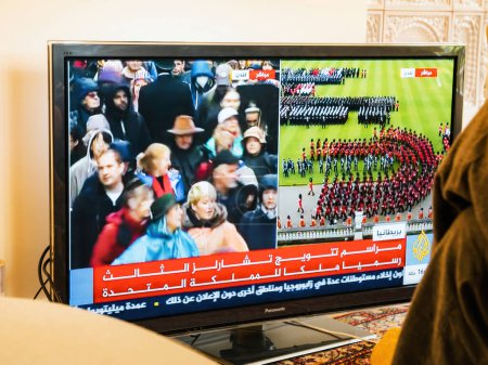 Téléchargez les photos : Paris, France - 6 mai 2023 : Une femme assiste au couronnement historique de Charles III et Camilla en tant que roi et reine sur la chaîne arabe Al Jazeera. - en image libre de droit