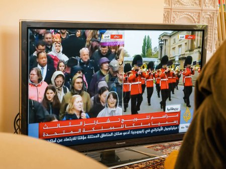 Téléchargez les photos : Paris, France - 6 mai 2023 : Une femme assiste au couronnement historique de Charles III et Camilla en tant que roi et reine sur la chaîne arabe Al Jazeera. - en image libre de droit