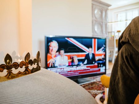 Téléchargez les photos : Paris, France - 6 mai 2023 : Une femme assiste au couronnement du roi et de la reine de Grande-Bretagne sur sa BBC News Channel. - en image libre de droit