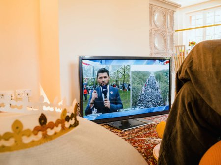 Téléchargez les photos : Paris, France - 6 mai 2023 : Une femme regarde attentivement le nouveau roi et la reine du Royaume-Uni couronnés sur TF1, première chaîne de télévision française. - en image libre de droit