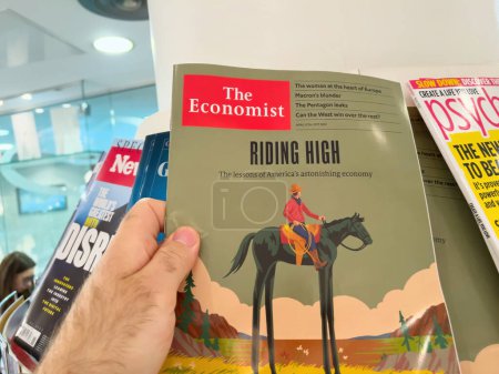 Téléchargez les photos : Londres, Royaume-Uni - 21 avril 2023 : Une main masculine détient le dernier numéro de The Economist, avec une couverture illustrée sur l'économie des Amériques. Journalisme et médias unissent leurs forces pour informer le - en image libre de droit
