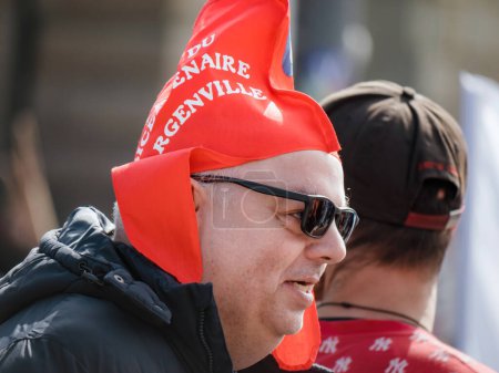 Téléchargez les photos : Strasbourg, France - 29 mars 2023 : Un adulte coiffé d'un chapeau rouge se tient fièrement au milieu d'une manifestation contre la réforme française des retraites. Il incarne l'esprit de résistance et d'espoir de changement. - en image libre de droit