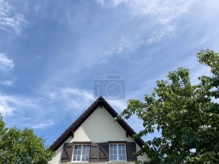 Téléchargez les photos : Une belle maison dans un village magique, avec son toit et son cerisier visibles depuis la vue à angle bas. Nuages s'étendent à travers le ciel au-dessus de cette structure construite située dans une résidence - en image libre de droit