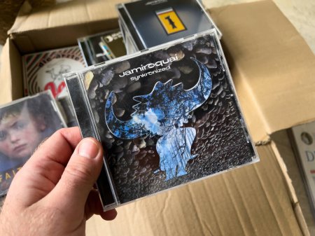 Téléchargez les photos : Paris, France - 1 Jan 13, 2023 : Un homme tient une boîte en carton rempli d'enregistrements médias classiques, sur le point de débloquer le Jamiroquai Syncronizes album CD audio. - en image libre de droit