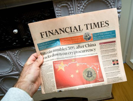 Photo for London, United Kingdom - May 20, 2021: POV male hand reading in room Financial Times newspaper with headline breaking news bitcoin tumbles 30 percent after China cracks down on cryptocurrency - Royalty Free Image