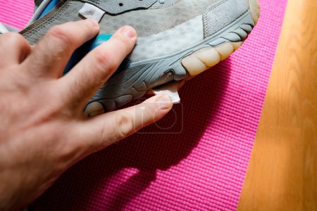 Foto de Un hombre inspecciona cuidadosamente un zapato de correr rasgado, su dedo tocando la tela desgastada y la suela del equipo deportivo de lujo. - Imagen libre de derechos