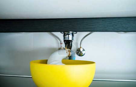 Téléchargez les photos : Un plombier nettoie avec diligence le siphon des lavabos dans une salle de bain bouchée de poils et de saleté sous l'évier. - en image libre de droit