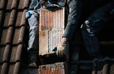 Foto de Dos constructores de techos trabajan juntos para renovar una antigua chimenea, asegurando que esté lista para la fría temporada de invierno. Primer plano de sus poderosas manos - Imagen libre de derechos