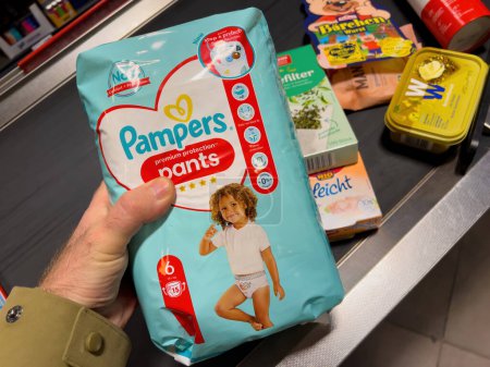 Téléchargez les photos : Francfort, Allemagne - 4 mars 2022 : Un homme tient un paquet de couches Pampers au comptoir de caisse dans un supermarché, prêt à acheter. - en image libre de droit
