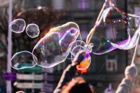 Foto de Un grupo de amigos divirtiéndose al aire libre en la ciudad, haciendo globos de jabón con sus manos. - Imagen libre de derechos