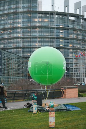 Téléchargez les photos : Un grand ballon écologique dirigeable vert se dresse devant le bâtiment du Parlement, Strasbourg étant inscrit en caractères gras. Les gens le préparent pour le lancement. - en image libre de droit