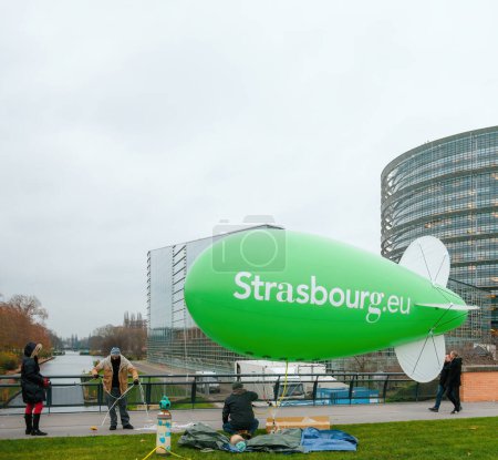 Téléchargez les photos : Les gens travaillent pour gonfler un grand ballon vert avec les mots Strasbourg inscrits devant le Parlement. Son but est d'attirer l'attention sur les questions environnementales. - en image libre de droit