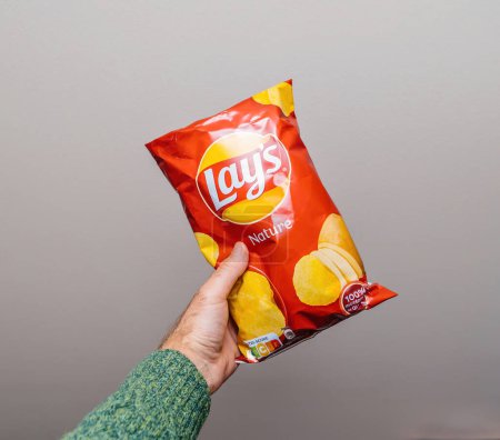 Photo for Lyon, France - May 24, 2023: A persons hand grasps a bright bag of Lays chips against an empty, gray background - delicious salt nature chips snack food - Royalty Free Image