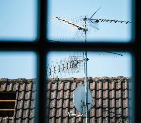 Téléchargez les photos : Une vue imprenable sur un toit carrelé bleu rempli de diverses antennes vues à travers une fenêtre voûtée, en cours de réparation. - en image libre de droit