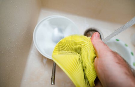 Photo for A person holds an yellow silicone sponge above a sink full of sparkling clean water, washing dishes with perfect POV. - Royalty Free Image