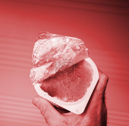 Téléchargez les photos : Une main saisit un récipient en plastique avec du yaourt moisi à l'intérieur. La croissance du mycélium et la pourriture fongique se forment dans le vaisseau. Un support ou un récipient pour couler ou former. - en image libre de droit