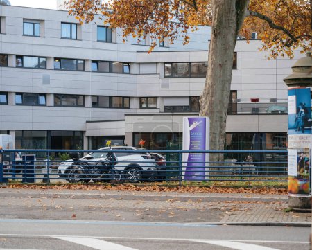 Foto de Estrasburgo, Francia - 22 de noviembre de 2022: Edificios residenciales y árboles alineados a lo largo de la acera en una zona urbana moderna. Un coche pasa como un hospicio para personas mayores y el espacio verde se ven cerca EHPAD - Imagen libre de derechos