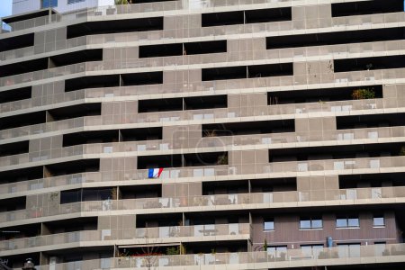 Téléchargez les photos : Un immeuble d'appartements français, avec un stade skyline en vue. Un match de championnat inspire le fanatisme alors que le drapeau national français tricolore vagues en hommage. - en image libre de droit