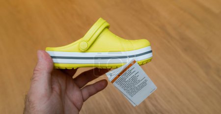 Photo for Paris, France - Jun 1, 2023: A childs hand holds a new, green and yellow Crocs shoe in a close-up view, with one person unboxing the childrens size footwear, showcasing the slippers. - Royalty Free Image