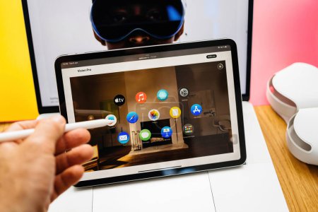 Photo for Paris, France - Jun 6, 2023: Hand holding pencil above tablet iPad Pro showcasing multiple apps and Apple Vision Pro mixed reality XR headset. Priced 3,499 USD - future of computing - Royalty Free Image
