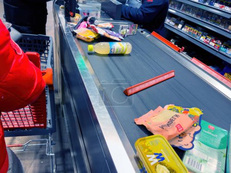 Foto de Alemania - 4 de marzo de 2023: Las personas que esperan en la cola cerca de una amplia gama de alimentos frescos y provisiones de despensa llenan el mostrador del supermercado alemán. Una verdadera escena de oferta y variedad para semanalmente - Imagen libre de derechos