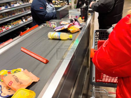 Téléchargez les photos : Allemagne - 4 mars 2023 : Vue latérale des clients qui attendent en file d'attente près d'une gamme diversifiée d'épiceries fraîches et de garde-manger remplit le comptoir du supermarché allemand. Une véritable scène d'offre et de variété - en image libre de droit