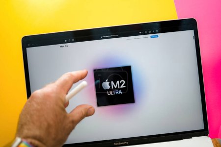 Téléchargez les photos : Paris, France - 6 juin 2023 : Pointant sur le nouveau M2 Ultra avec 24-core 60-core GPU et 32-core neural engine - Table de salle créative avec page web d'Apple sur ordinateur portable vitrine - main de l'utilisateur interagissant - en image libre de droit