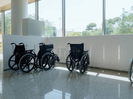 Foto de En el aeropuerto, sillas de ruedas estacionadas en el interior por la ventana, mostrando el equipo médico y las instalaciones de transporte. No hay gente presente. Énfasis en la accesibilidad y las diferentes capacidades. - Imagen libre de derechos