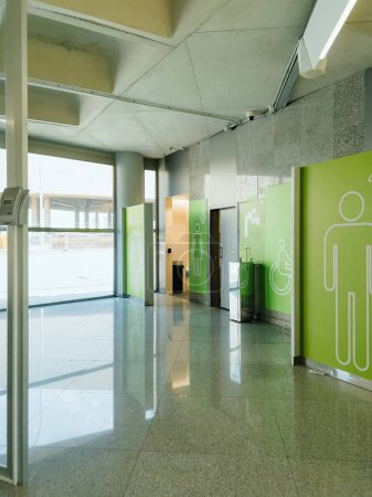 Photo for Contemporary elegant airport toilet in Palma de Mallorca, featuring minimalist design, green color scheme, concrete floors, marble walls, and inviting lighting. Convenient signage guides visitors. - Royalty Free Image